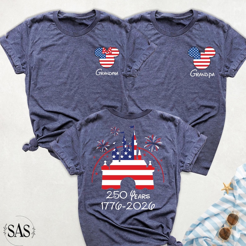May include: Three navy blue t-shirts with patriotic designs. Two shirts feature a Mickey Mouse head with red, white, and blue accents and the words "Grandma" and "Grandpa." The third shirt displays a castle with the text "250 Years 1776-2026."