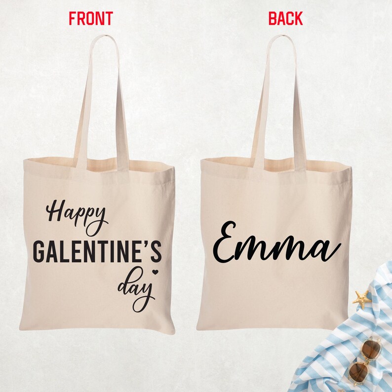 May include: A beige canvas tote bag with long handles. The front of the bag says "Happy Galentine's Day" in black script. The back of the bag has the name "Emma" in black script.