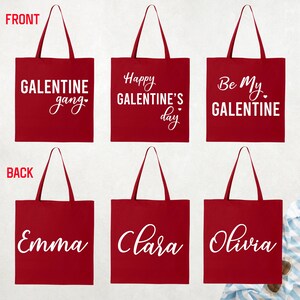 May include: Red tote bags with white text. The front of the bags say "GALENTINE gang", "Happy GALENTINE'S day", and "Be My GALENTINE". The back of the bags say "Emma", "Clara", and "Olivia".