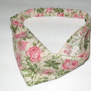 May include: A floral headband featuring a cream-colored fabric adorned with pink roses and green leaves. The headband has an elastic band for a comfortable fit and a stylish, twisted front design.