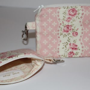 May include: Two small, open floral print pouches with white zippers and silver-tone hardware. The larger pouch is rectangular with a pink and white floral pattern. The smaller pouch is open, revealing a floral interior.