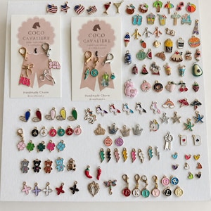 May include: A collection of assorted metal enamel charms featuring various shapes including food, animals, letters, symbols, and holiday themes. Two display cards labeled Coco Cavaliere with attached lobster clasps and charms are included.