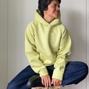 Short hair woman sitting on a wood stool, wearing an oversize hoodie. Without logos. Color citric yellow