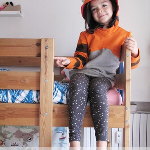 May include: A child wearing a tiger-themed hoodie and star-patterned leggings sits on a wooden bunk bed. The hoodie is orange and gray with black stripes and white ear details. The text on the image says "The girl in the picture is wearing size 7 years."
