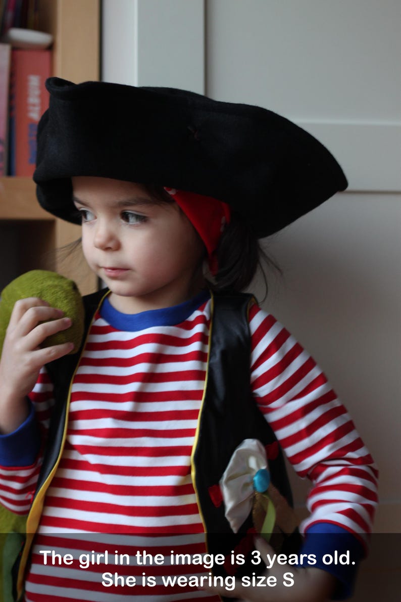 May include: A child in a pirate costume, including a black hat, red and white striped shirt, and a black vest. The outfit includes a red bandana and a green prop. The text in the image says the child is 3 years old and wearing size S.