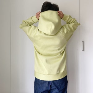 Woman wearing an oversize hoodie. Without logos. Color citric yellow. View from the back