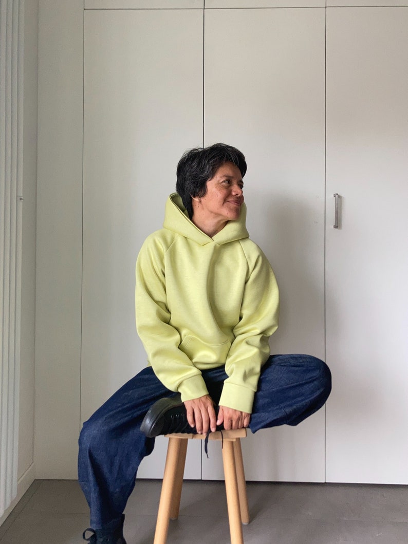 Short hair woman sitting on a wood stool, wearing an oversize hoodie. Without logos. Color citric yellow