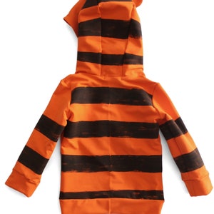 May include: Orange and black striped hooded sweatshirt with attached ears. The sweatshirt features a full-length zipper and ribbed cuffs. The design resembles a tiger.