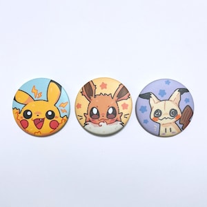 Pode incluir: Três botões redondos e coloridos com personagens de desenhos animados. O primeiro botão tem um personagem amarelo com bochechas vermelhas e um fundo azul. O segundo botão tem um personagem marrom com uma área branca e fofa e um fundo laranja. O terceiro botão tem um personagem creme com um fundo roxo.