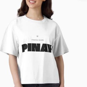 Könnte beinhalten: Weißes T-Shirt mit dem Wort "PINAY" in fetten schwarzen Buchstaben auf der Vorderseite. Oberhalb des Wortes steht der Satz "mixed but double". Das Shirt hat kurze Ärmel und einen Rundhalsausschnitt.