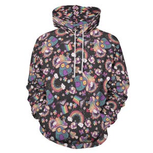 Peut inclure: Un sweat à capuche noir avec un motif coloré de maisons champignons, d'arcs-en-ciel et de fleurs. Le motif comprend le drapeau de la fierté LGBTQ+. Le sweat à capuche a une capuche à cordon et une poche avant.