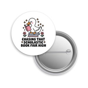 May include: A white button pin with a cartoon duck reading a pink book, atop a stack of books, with flowers and stars. The text reads "Chasing That Scholastic Book Fair High."