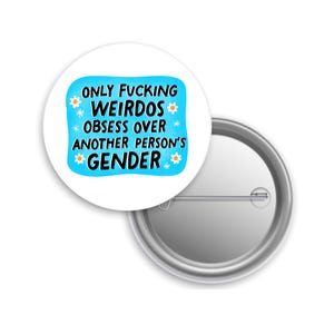 May include: A white button pin with the text "ONLY FUCKING WEIRDOS OBSESS OVER ANOTHER PERSON'S GENDER" in black, with a light blue background and daisy accents. The pin is round and has a metal backing.