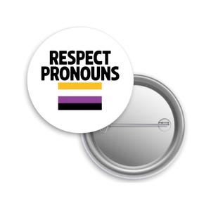 May include: A white button with the text "RESPECT PRONOUNS" in black. Below the text is a horizontal bar in yellow, purple, and black. The button is round and has a metal pin back.