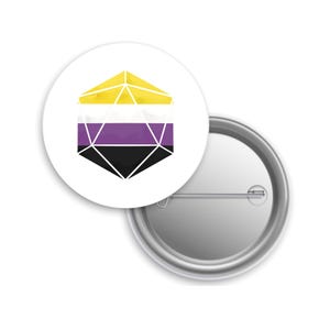 May include: A white button pin with a non-binary pride flag design. The design features a geometric shape with yellow, white, purple, and black sections. The pin is round with a metal backing and a safety pin closure.