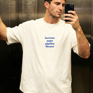 May include: A white short-sleeved t-shirt featuring the blue text "lacrosse segue pipeline finance" printed in a centered, stacked format on the chest. The garment has a crew neckline and a relaxed fit, providing a clean and simple aesthetic.