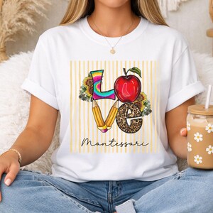May include: A white t-shirt featuring a graphic design with the word LOVE, where the L is tie-dye, the O is a red apple, the V is two yellow pencils, and the E has a leopard print. Sunflowers surround the letters, and the text Montessori is below.