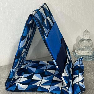 May include: A blue and white geometric patterned fabric book stand. The stand is triangular in shape and has a solid blue fabric on the outside. The stand is designed to hold a book or tablet.