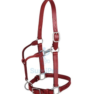 Pode incluir: Um cabresto de cavalo de couro vermelho com ferragens de metal prateado. O cabresto possui correias ajustáveis, fivelas e anéis para um ajuste seguro. O design inclui uma testeira, uma focinheira e uma barbela, todos conectados com costuras resistentes.