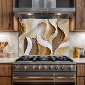May include: A kitchen backsplash panel featuring a layered, abstract design of flowing, curved ribbons in shades of cream, beige, tan, and dark brown. The smooth, undulating lines create a sense of depth and movement behind a stainless steel stove.