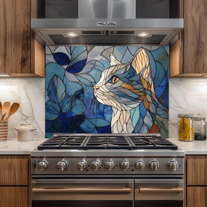 Puede incluir: Un protector contra salpicaduras de cocina con un diseño de gato estilo vidriera. El gato está representado en tonos azules, blancos y naranjas, sobre un fondo de hojas azules. El protector está instalado detrás de una cocina de gas de acero inoxidable.