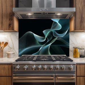 Puede incluir: Una placa protectora de cocina con un fondo negro y un diseño abstracto y fluido en tonos turquesa y blanco. Se instala detrás de una cocina de gas de acero inoxidable y debajo de una campana extractora de acero inoxidable. Armarios de madera y encimera de mármol.