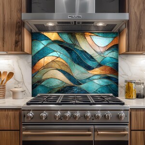 Puede incluir: Un protector contra salpicaduras de cocina con un diseño de vidriera que presenta olas fluidas en tonos turquesa, azul y cobre. Se instala sobre una estufa de gas de acero inoxidable y debajo de una campana extractora.