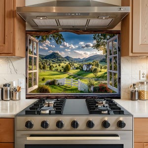 May include: A kitchen splashback panel featuring a printed landscape scene of a green valley, rolling hills, and a white house viewed through an open window frame with wooden trim, positioned behind a stainless steel gas stove and range hood.