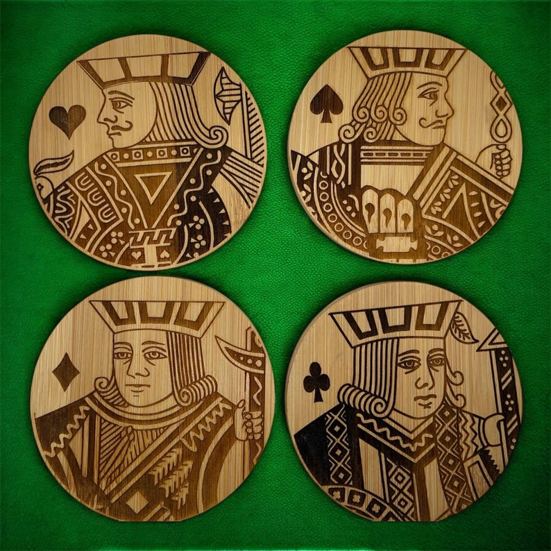 May include: A set of four circular bamboo coasters, each featuring a laser-engraved design of a different playing card king. The designs include the king of hearts, spades, diamonds, and clubs, showcasing intricate line work and wood grain texture.