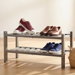 May include: A two-tiered gray wooden shoe rack displays various footwear. The top shelf holds burgundy sneakers and brown leather loafers. The bottom shelf features blue sneakers. A woven basket sits to the side, adding a decorative touch.