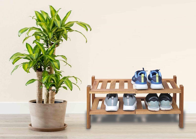 Puede incluir: Un zapatero de madera de dos niveles con cuatro pares de zapatillas deportivas. A la izquierda, una planta de Dracaena en maceta con hojas verdes y amarillas. Las zapatillas son azules, grises y negras.