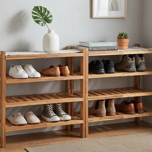 Puede incluir: Zapatero de madera con tres estantes, que muestra varios zapatos. El estante es de madera de color marr&oacute;n claro y tiene un dise&ntilde;o de listones. Un jarr&oacute;n blanco con una hoja verde y una peque&ntilde;a planta en maceta est&aacute;n encima.
