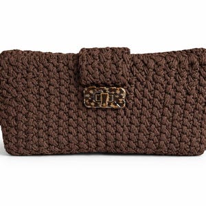 May include: A brown crocheted clutch with a rectangular shape. The bag features a textured surface and a decorative clasp with a tortoiseshell pattern. The clutch is a stylish accessory for carrying essentials.