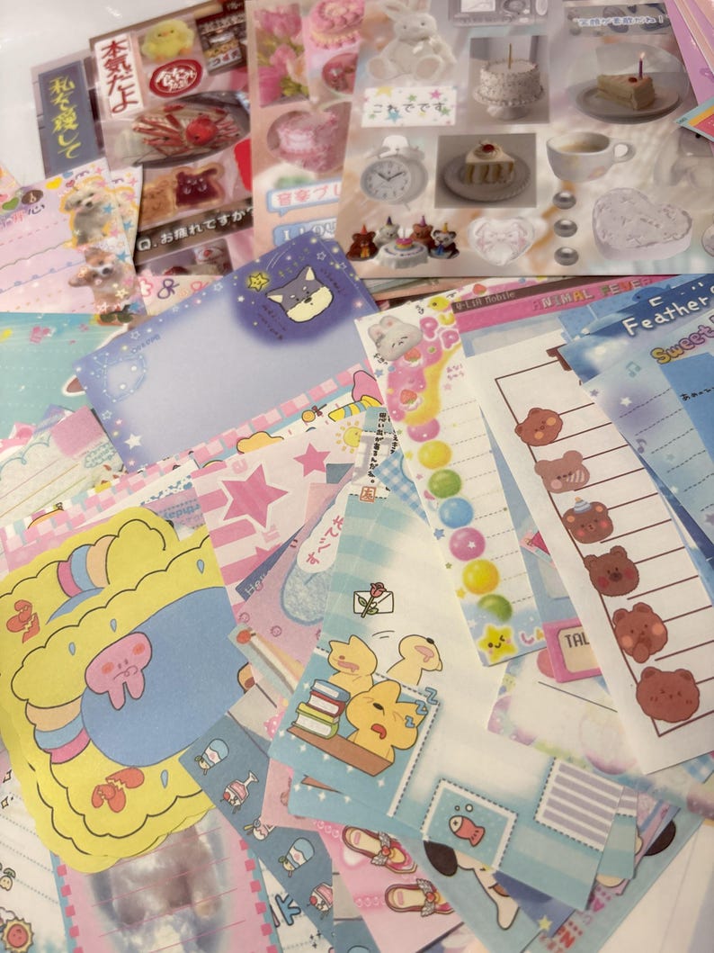 May include: A selection of colourful stationery items, including stickers, notepads, and decorative papers. The designs feature cute illustrations of animals, cakes, and stars, with pastel colour schemes. Some items have Japanese text.