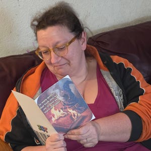 May include: A person reading a greeting card with the text "So many spells in that book, and not one of them was Ward off Reaper." The card features an illustration of a wizard's hat and a burning book. The card has a Zest logo.