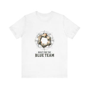 May include: A white short-sleeve t-shirt featuring a central graphic of five hands linked in a circle over a technical blueprint grid. Below the graphic, the text reads BUILT FOR THE BLUE TEAM in a bold, dark, sans-serif font style.