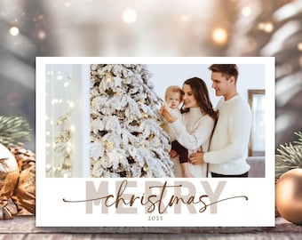 May include: A white Christmas card with a family photo in front of a decorated Christmas tree. The card has the words "MERRY christmas 2025" in brown lettering. The family is wearing white sweaters.