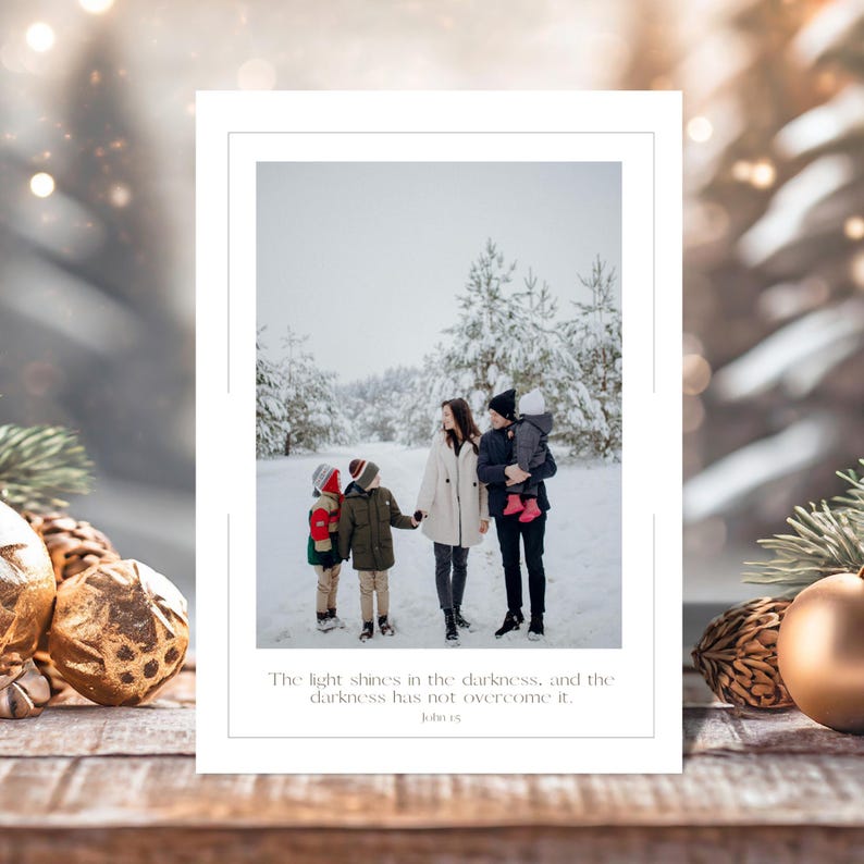 May include: A white greeting card with a family portrait in a snowy forest. The family of five is dressed in winter attire. The card includes the text: "The light shines in the darkness, and the darkness has not overcome it. John 1:5."
