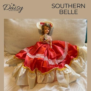 May include: A vintage doll in a red satin dress with white lace trim and a wide cream-coloured skirt. The doll has a matching hat and is labelled "Southern Belle". The Daisy Retro Designs logo is in the upper left corner.