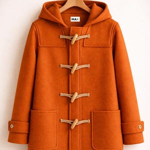Può includere: Un montgomery con cappuccio color arancio bruciato dotato di quattro chiusure a olivetta in legno chiaro con asole in corda, due ampie tasche frontali applicate e polsini regolabili con bottoni. L'etichetta interna riporta il testo MAX.