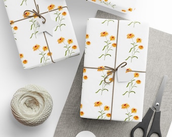 Puede incluir: Varios regalos envueltos con un estampado floral blanco de flores amarillas y tallos verdes. Los regalos están atados con hilo marrón y tienen etiquetas blancas. También hay una madeja de hilo, tijeras y etiquetas en blanco.