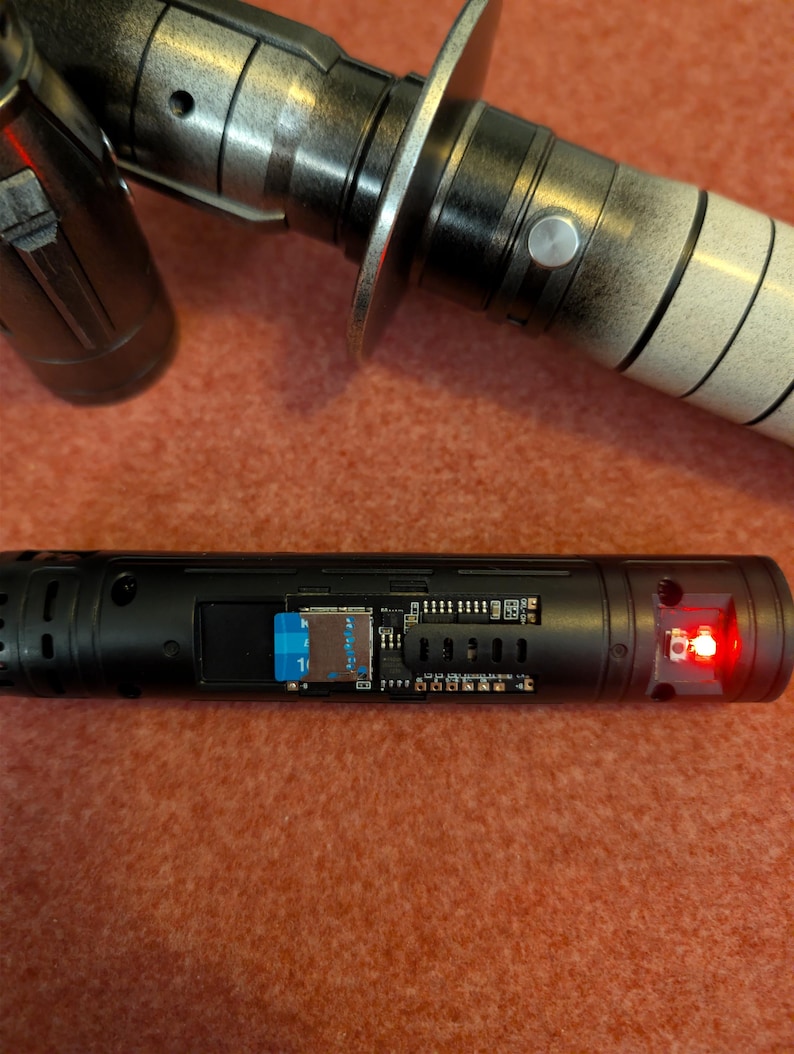 Puede incluir: Una empu&ntilde;adura de sable de luz negra y plateada con una luz roja en el extremo. La empu&ntilde;adura tiene un dise&ntilde;o detallado con un protector de hoja plateado. La secci&oacute;n inferior de la empu&ntilde;adura tiene una ranura para una tarjeta SD.