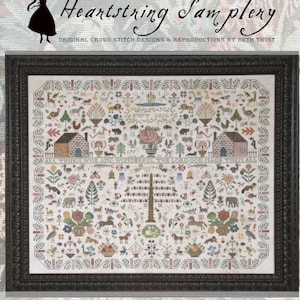 May include: A framed cross-stitch sampler featuring the text "Heartstring Samplery" and "All Things Wise + Wonderful." The intricate design includes houses, animals, and floral motifs, set within a black frame.