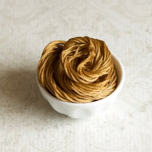 May include: A white ceramic bowl filled with a ball of golden brown yarn.