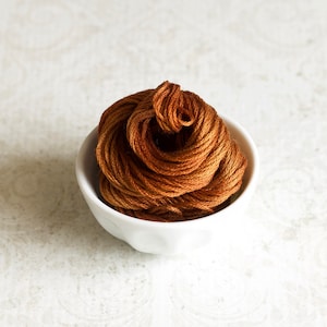 May include: A white ceramic bowl filled with a large amount of brown embroidery floss.