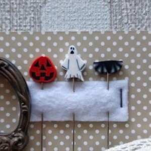 May include: Four Halloween themed sewing pins with white felt backing. The pins feature a ghost, a pumpkin, a bat, and a spider.