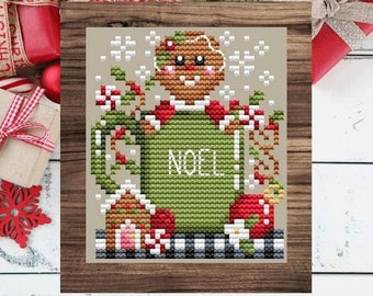 May include: Cross stitch pattern featuring a gingerbread person holding a green mug with the word "NOEL" on it. The mug is surrounded by candy canes, holly, and a small gingerbread house. The pattern is set against a beige background with snowflakes.