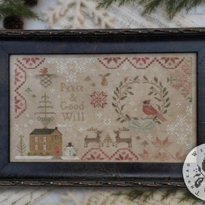 May include: A framed cross-stitch design with a winter theme. The artwork includes the words "Peace & Good Will", a house, deer, a cardinal, and snowflakes. The frame is dark brown.
