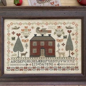 May include: A framed cross-stitch embroidery depicting a red house with a green roof, two trees, a bird, and a deer. The embroidery includes the alphabet, numbers, and the year 2022.