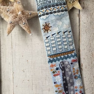 May include: A blue and white Christmas stocking with a nautical theme. The stocking features a whale, fish, and an anchor. The top of the stocking has a sun and birds.